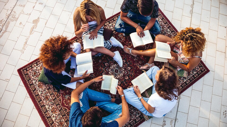 Un groupe d'adolescent assis par terre sur un tapis qui sont en train de livre des livres.