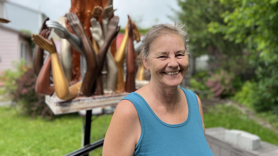 Une femme souriante devant une sculpture.