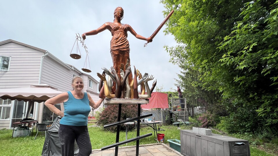 Une femme souriante aux côtés d'une grande sculpture d'une femme qui tient une balance et une épée.
