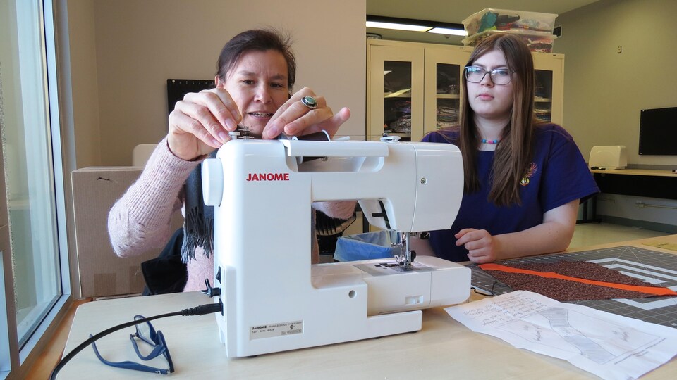 Une jeune femme et son enseignante qui utilisent une machine à coudre.