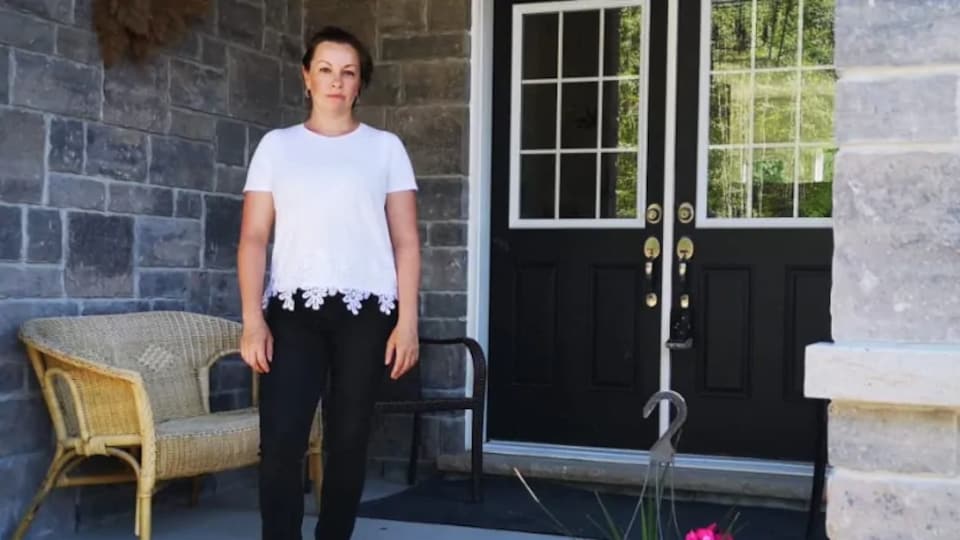 Une femme pose devant la porte d'entrée de sa maison.