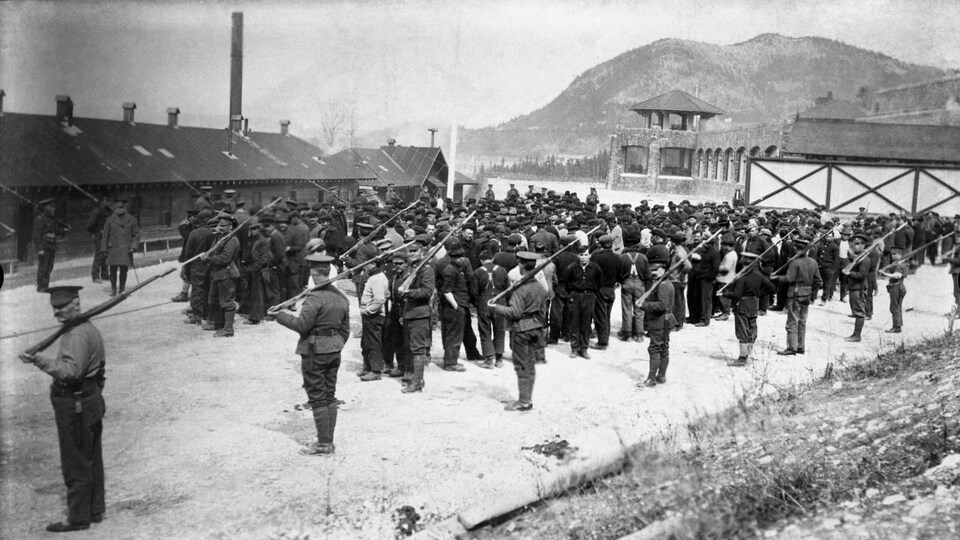 Photographie d'archive de soldats qui entourent un groupe de personnes sur un grand terrain.