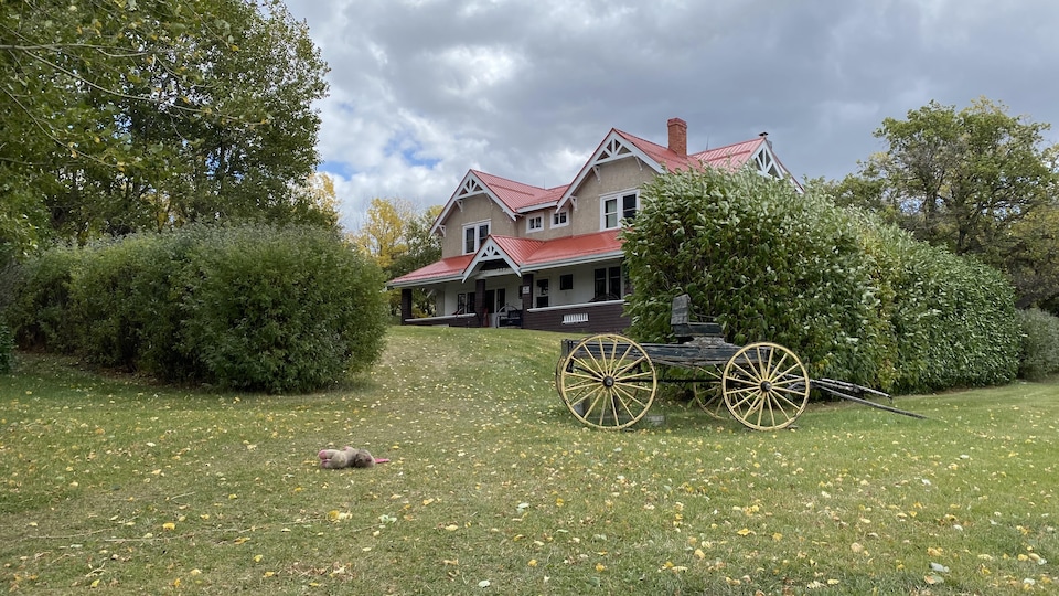 La maison Reesor a un toit en métal rouge et il y a un vieux wagon stationné devant la maison.