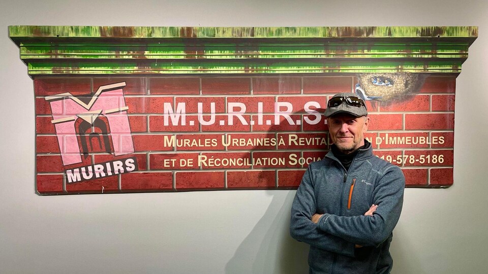 Serge Malenfant devant une pancarte indiquant M.U.R.I.R.S.