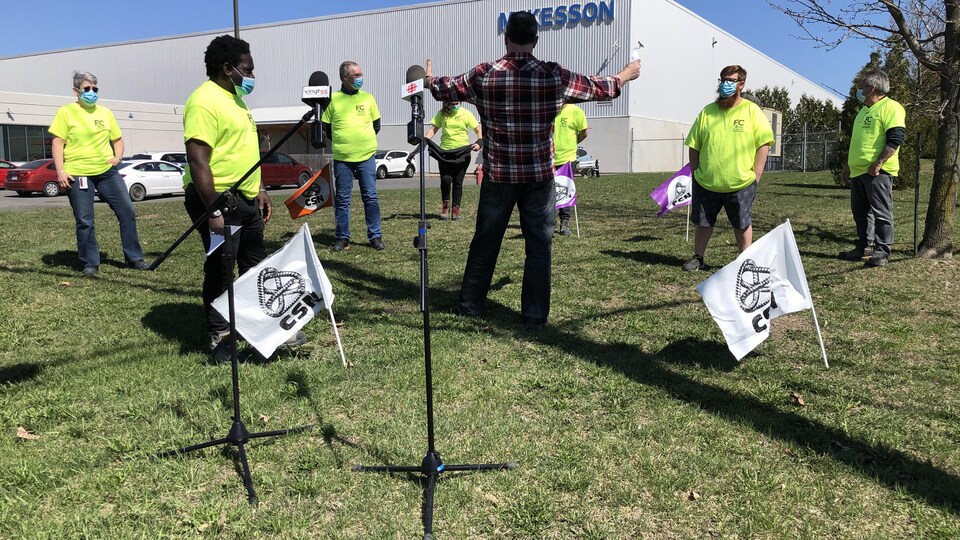 Des travailleurs portent un chandail jaune devant un édifice de McKesson.
