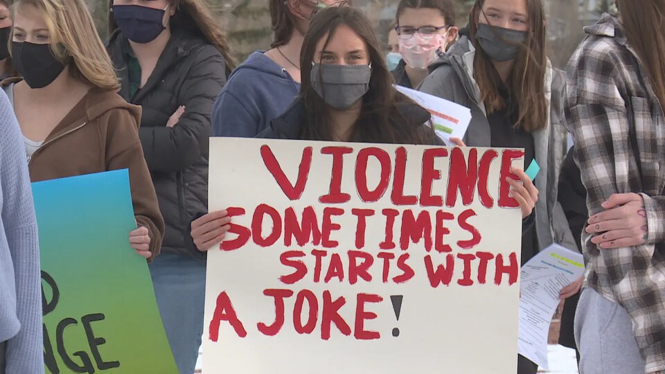 Une jeune femme tenant un panneau sur lequel est inscrit un slogan contre les violences sexuelles. 