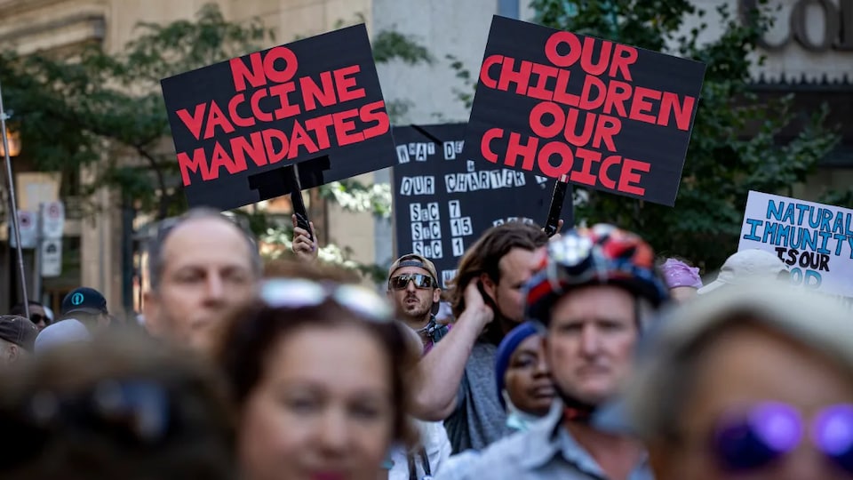 Des personnes manifestent et certaines tiennent des pancartes montrant leur opposition aux politiques sur la vaccination.