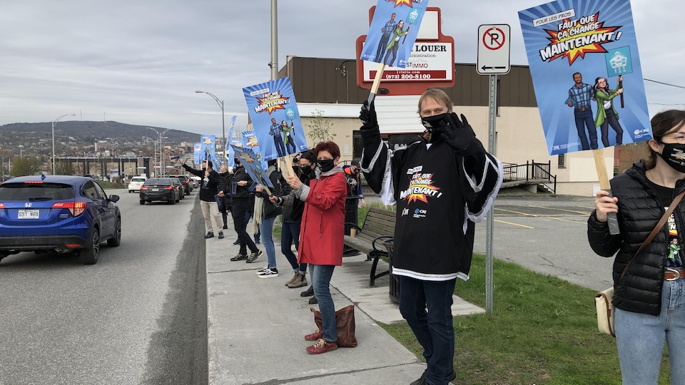 Des professionnels de l'éducation présentent leurs affiches de contestation sur le trottoir.