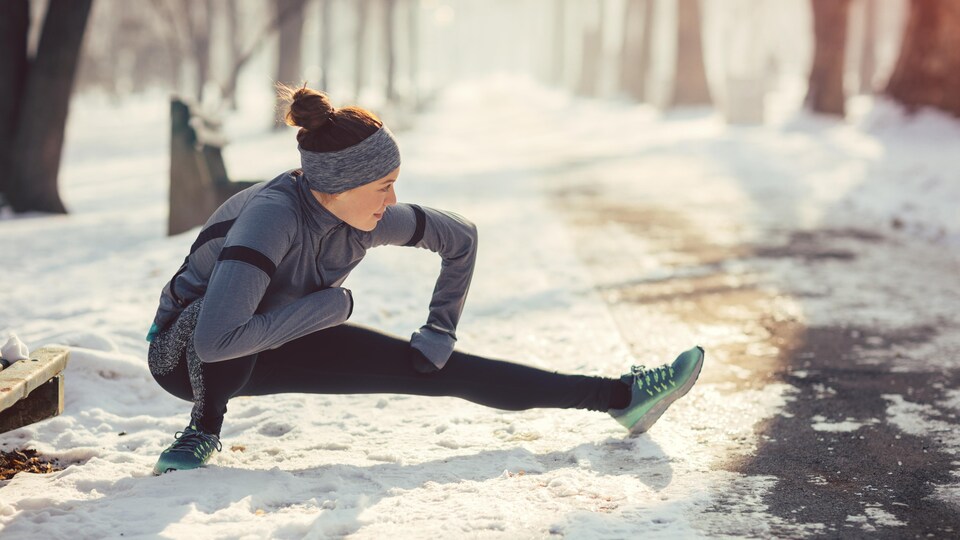 Une femme s'étire sur une piste enneigée avant de faire de la course à pied.