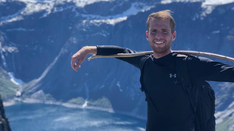 Un homme sourit sur le sommet d'une montagne.