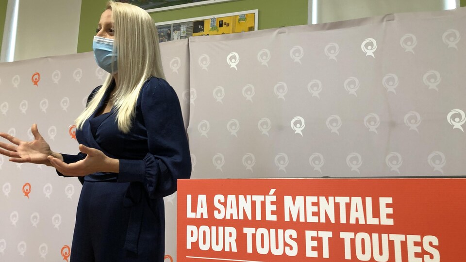 Mélissa Généreux s'adresse à la foule tout près d'une affiche aux couleurs de Québec solidaire qui met l'accent sur l'importance de la santé mentale.