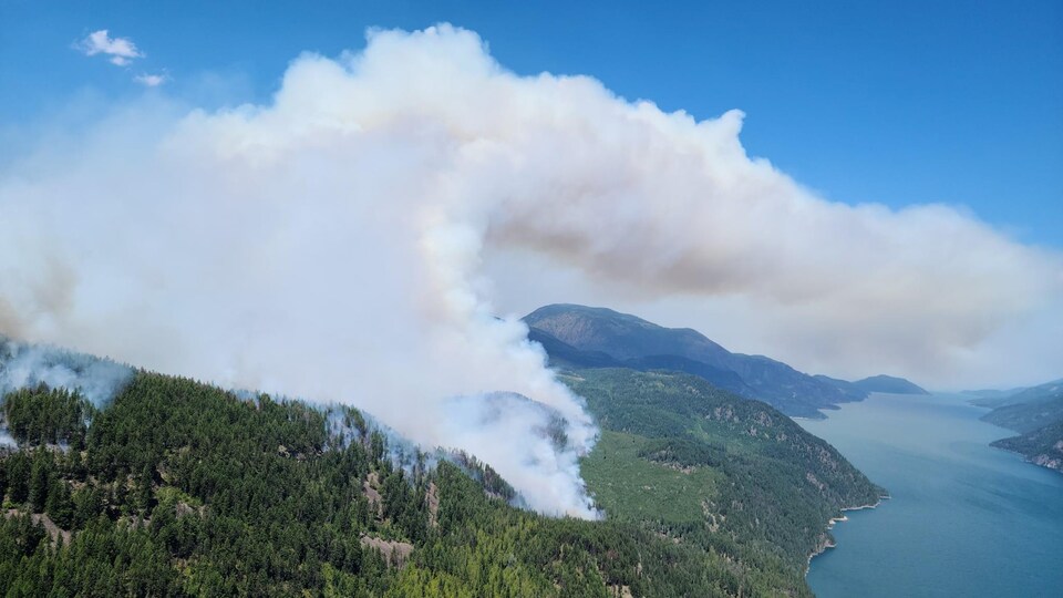 Un nuage de fumée part d'une zone de montagne au bord d'un lac.