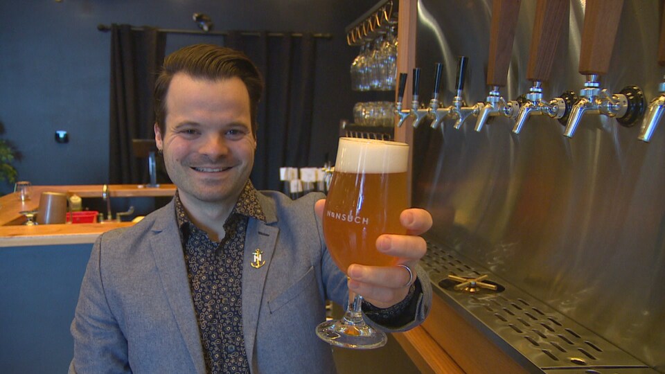 Dans une microbrasserie, un homme souriant présente un verre de bière.