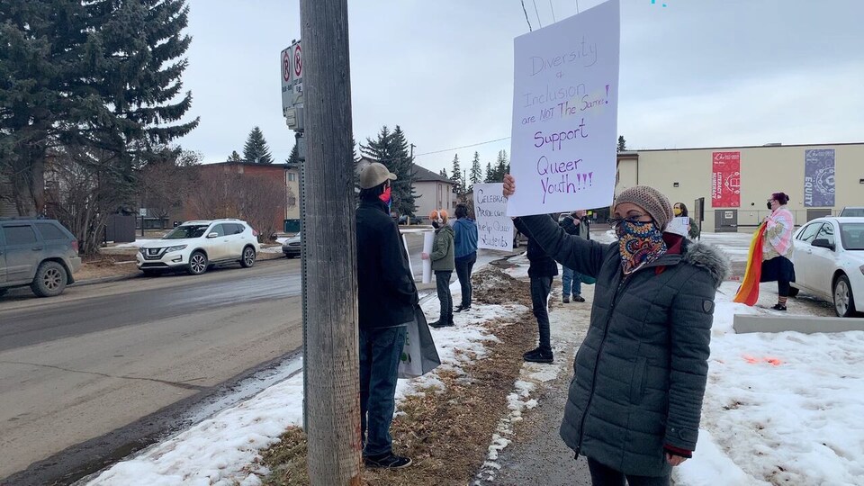 Des manifestants sur le trottoir brandissent des pancartes aux slogans LBTQ+ à Red Deer.