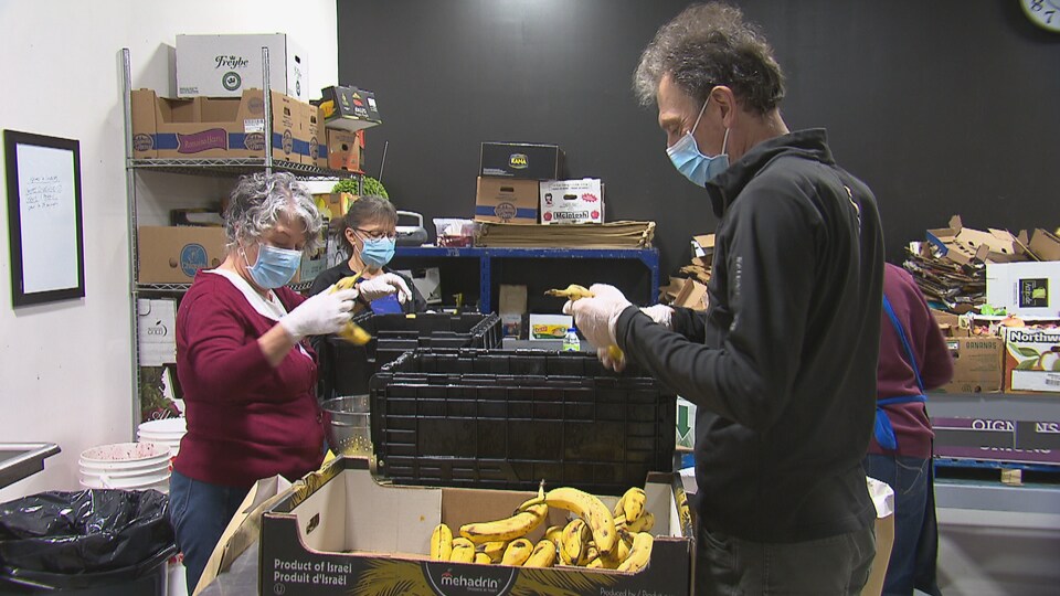 Trois bénévoles ouvrent des boîtes de nourriture, et en sortent notamment des bananes.