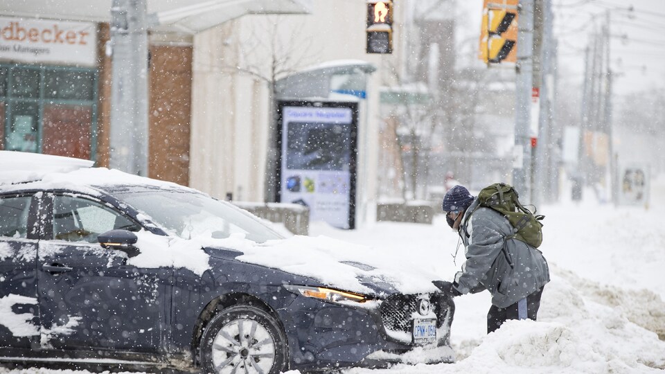 Un homme pousse une voiture enlisée dans la neige.