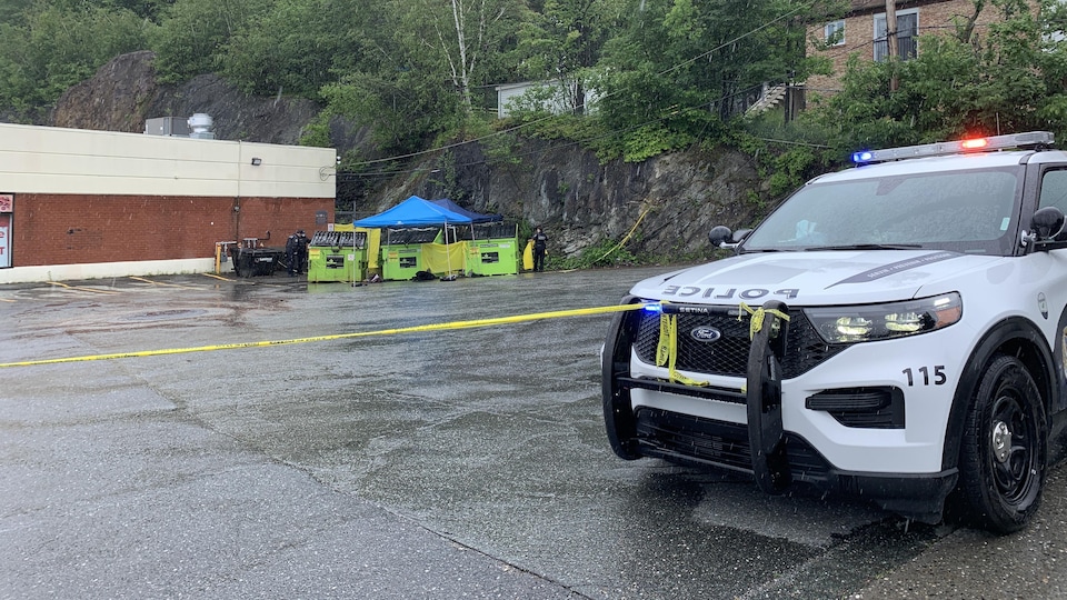 Un véhicule du Service de police de Sherbrooke attaché à un ruban définissant le périmètre. Trois conteneurs sont au centre de la scène.
