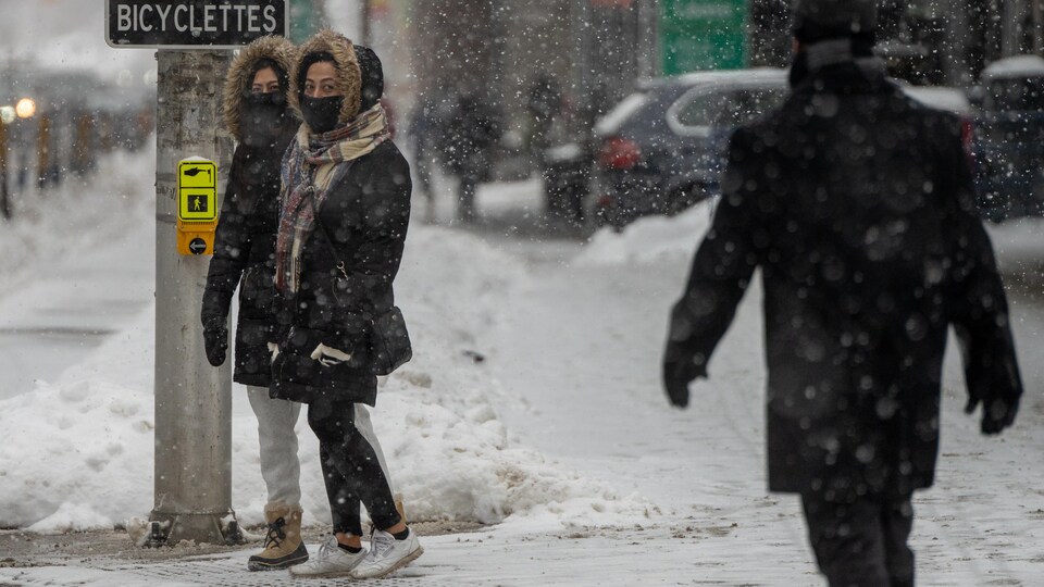 Deux personnes avec un masque sur le visage attendent de traverser la rue à Ottawa, en hiver.