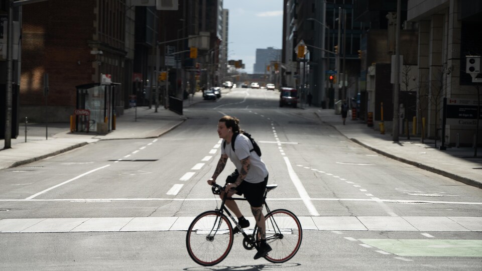 Un homme à vélo traverse la rue au centre-ville d'Ottawa.