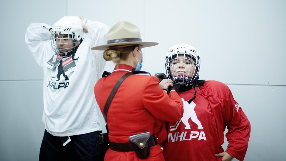 Une agente de la GRC aide un jeune à ajuster son équipement de hockey.