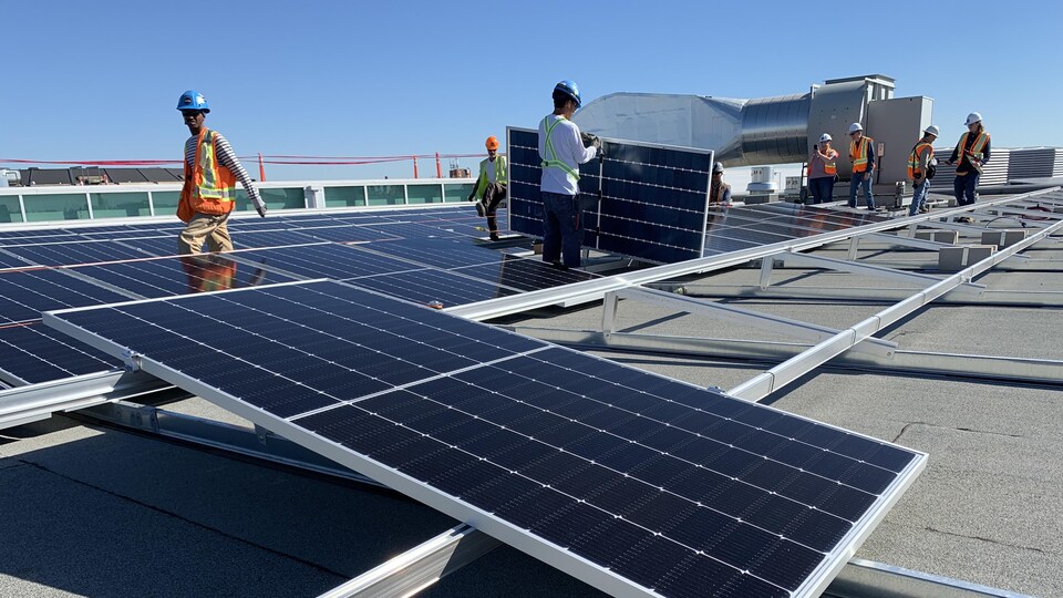 Travailleurs manipulant des panneaux solaires noirs qu'ils installent sur des structures métalliques argentées par une journée ensoleillée.
