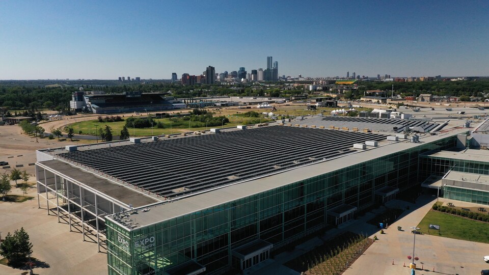 Plan aérien de panneaux solaires noirs montés sur une structure métallique argentée sur un toit en béton gris avec en arrière plan le centre-ville d'Edmonton par une journée ensoleillée d'été, le 18 août 2022.
