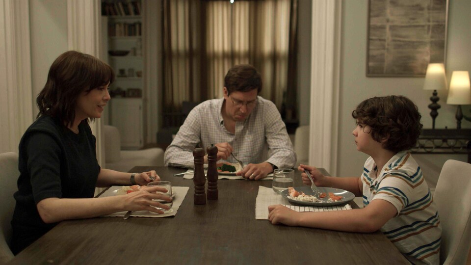 Une famille composée d'une femme, d'un homme et d'un jeune garçon assis à une table en train de manger un repas.