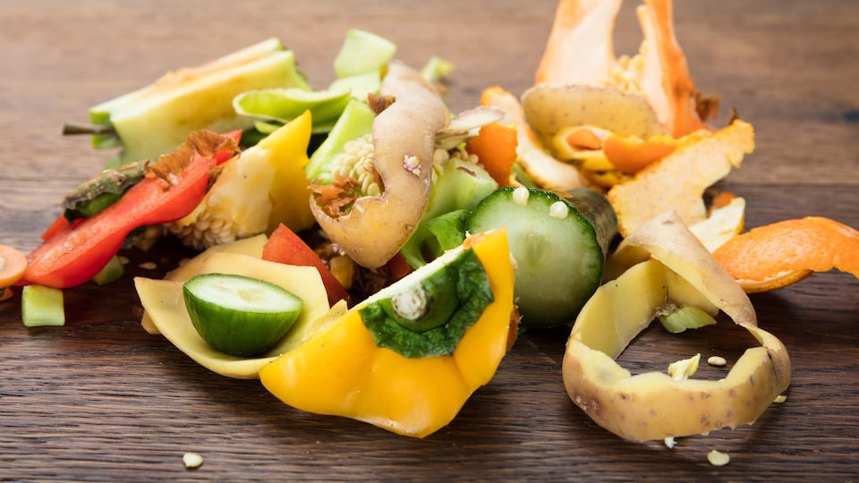 Des pelures de différents légumes sont déposées sur une table en bois.