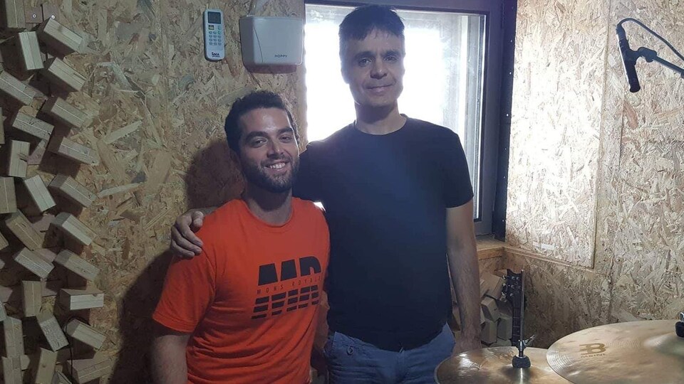 Deux hommes se tiennent par les épaules devant une batterie (percussion).