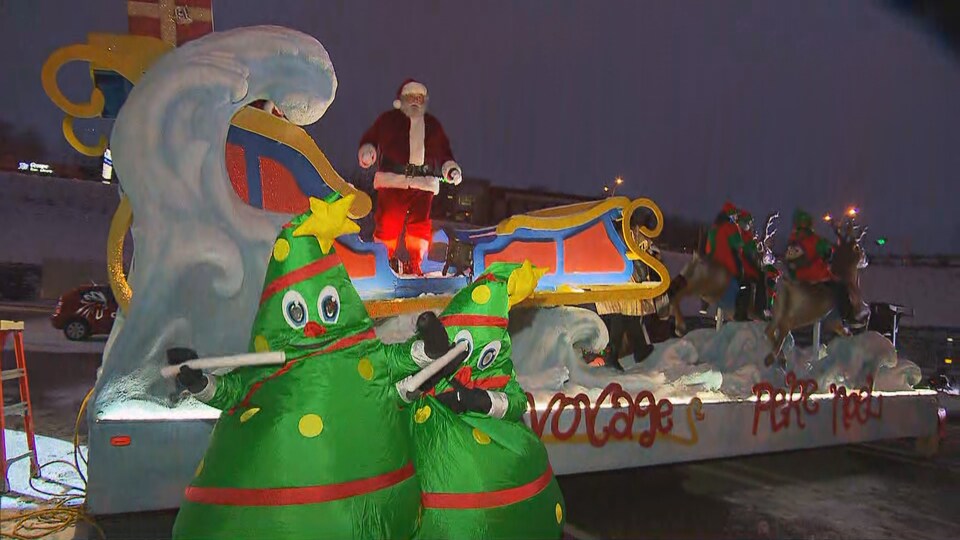 Le père Noël et tous ses rennes sur un char allégorique. Deux sapins dansent devant le char.