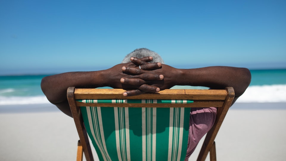 Vue de dos d'un homme assis sur une chaise de plage avec les mains croisées derrière sa tête.