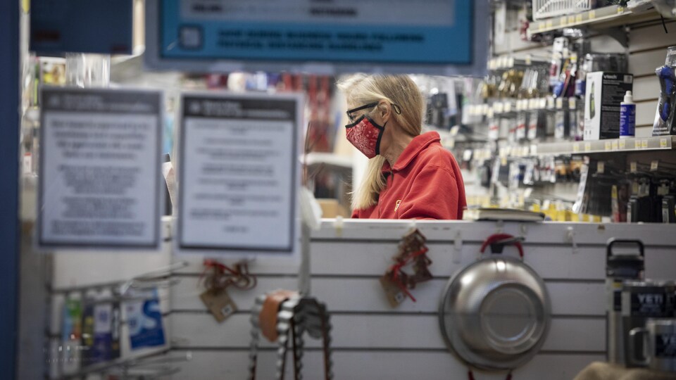 Une femme masquée tient le comptoir d'un magasin.