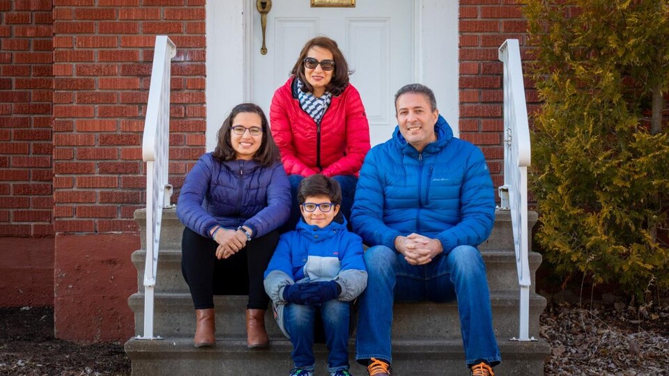 Une famille de quatre personnes est assise dans les marches de leur petit perron.