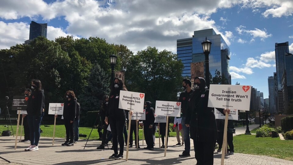 Plusieurs personnes vêtues de noir tiennent des écriteaux demandant la vérité autour de l'écrasement du vol PS752.