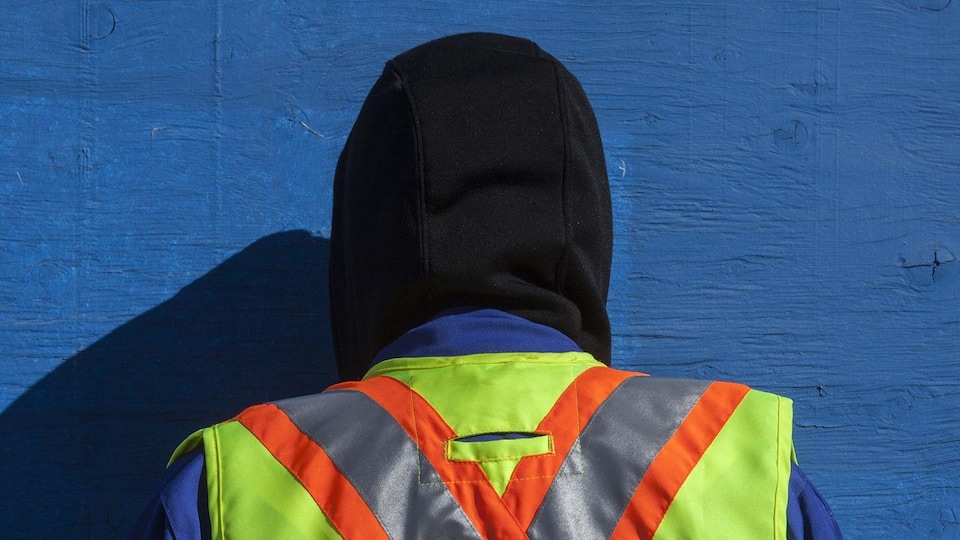 Personne de dos, avec un veste de visibilité. Face à cette personne un mur bleu.