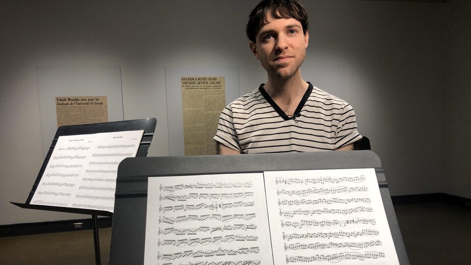Entouré de partitions de musique, un homme regarde la caméra.