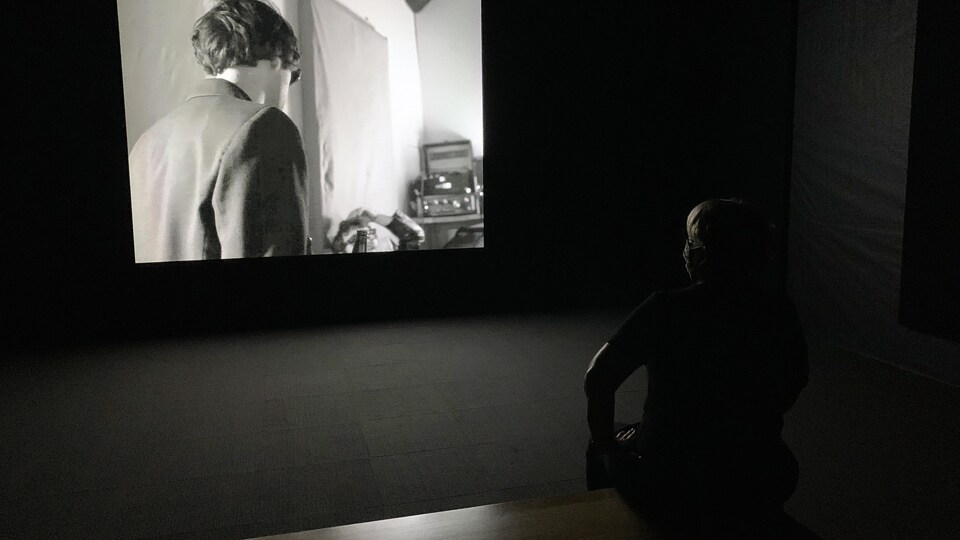 Une personne assise devant un écran de projection dans une pièce sombre.