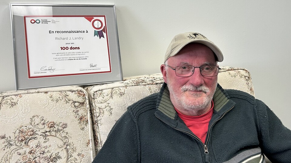 Richard Landry assit sur un canapé avec le certificat qu'il a reçu de la Société canadienne du sang.