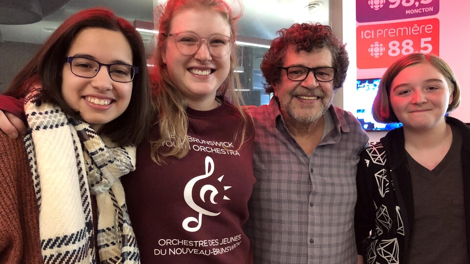 Trois jeunes femmes et un homme sont debout et sourient.