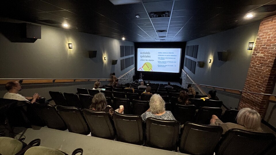 Une foule assise dans une salle de cinéma devant une présentation des activités offertes au Salon du livre de l'Estriere