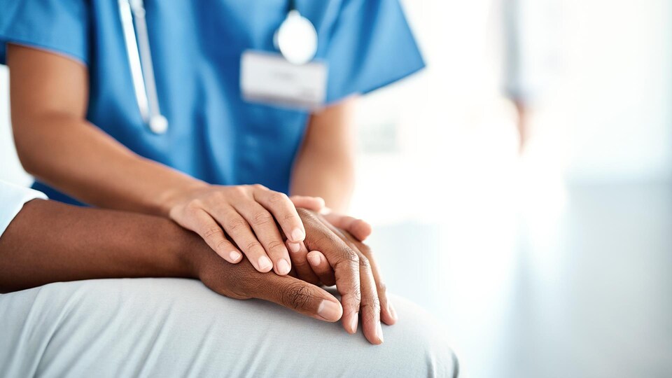 Gros plan des mains d'une personne en habits d'infirmière qui tient les mains d'une autre personne couchée.