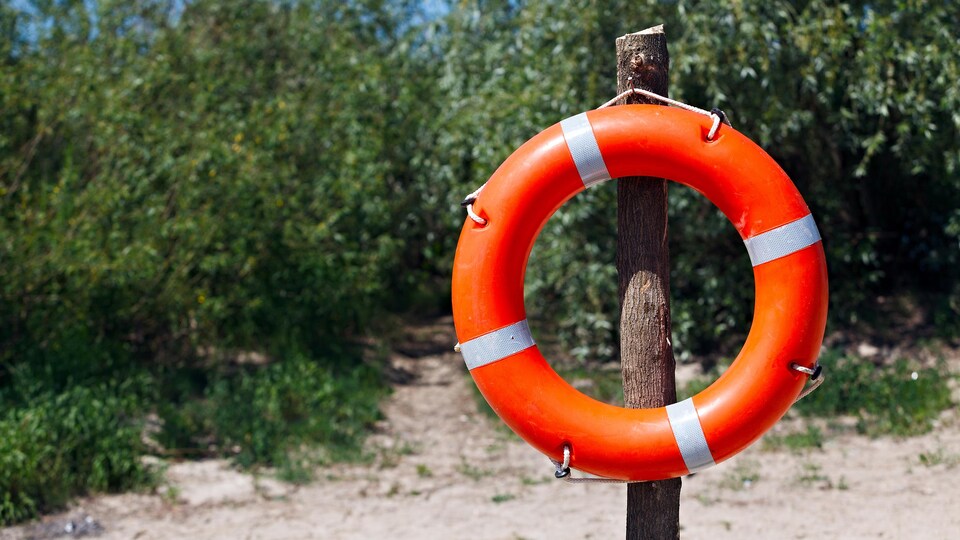 Une bouée de sauvetage accrochée sur un poteau de bois sur le bord d'une plage.