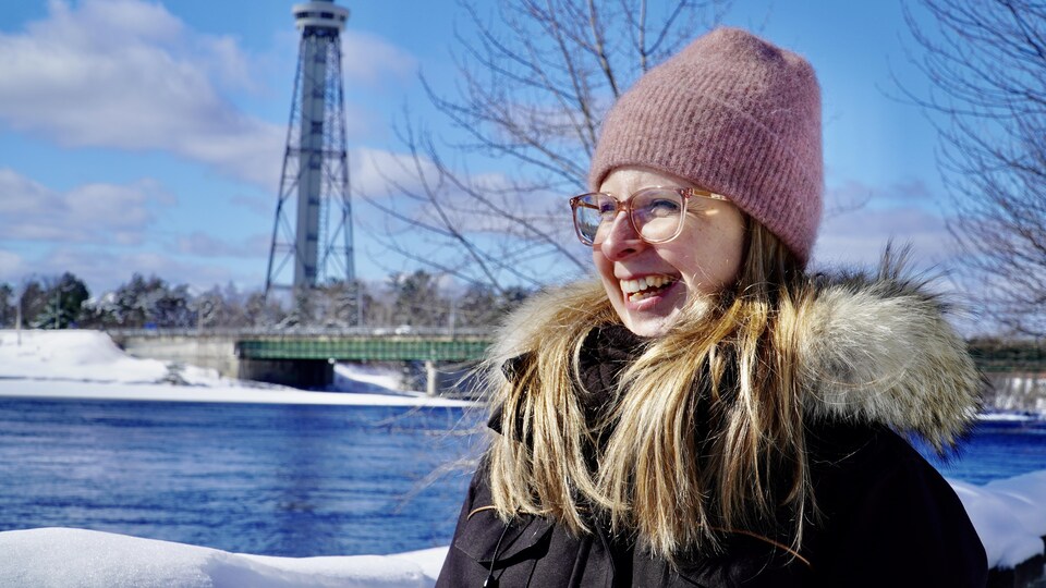 Jeune femme souriante devant une rivière l'hiver.