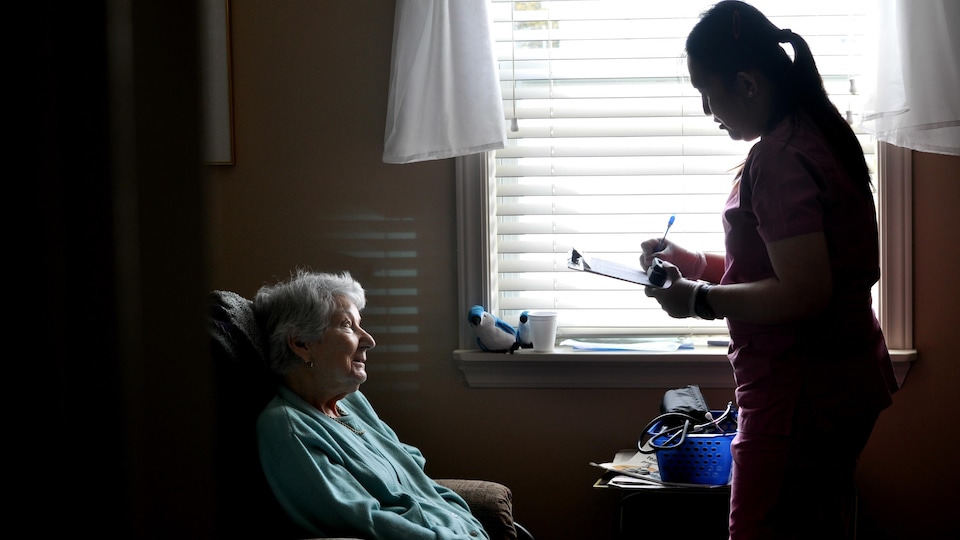 Une travailleuse en foyer note dans un dossier des informations au sujet de sa patiente, assise dans un fauteuil devant elle.
