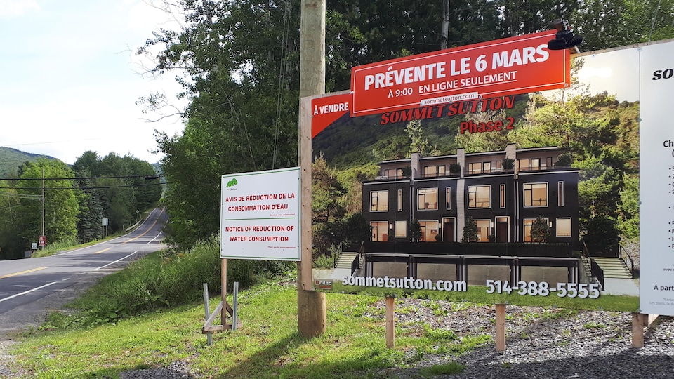 Une affiche en bord de route demande de réduire la consommation d'eau. À côté, une affiche fait la promotion d'un nouveau développement immobilier.