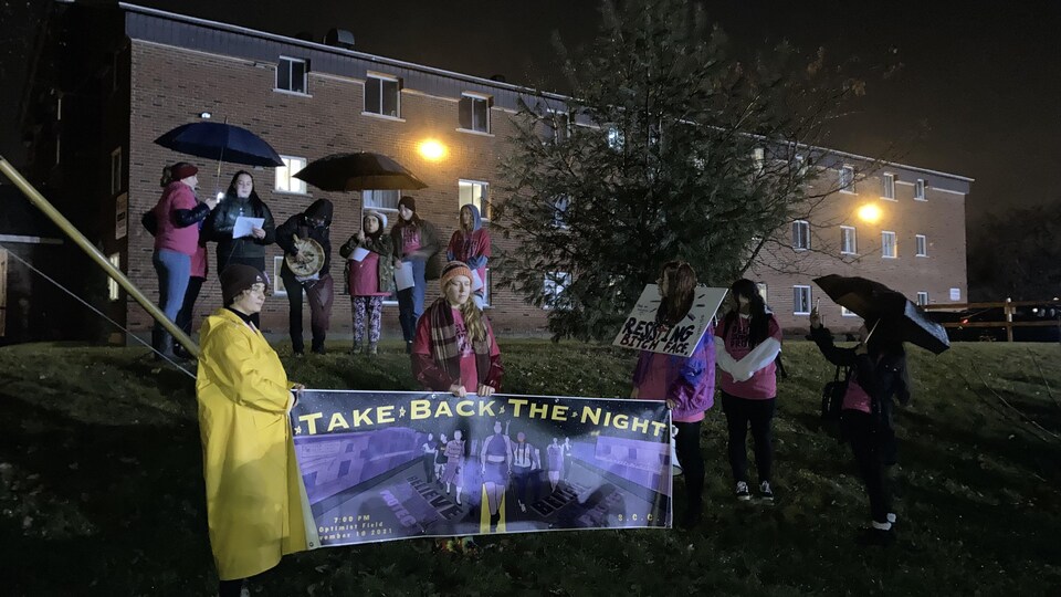 Des étudiantes parlent devant la foule. Elles tiennent une bannière qui indique "take back the night". 