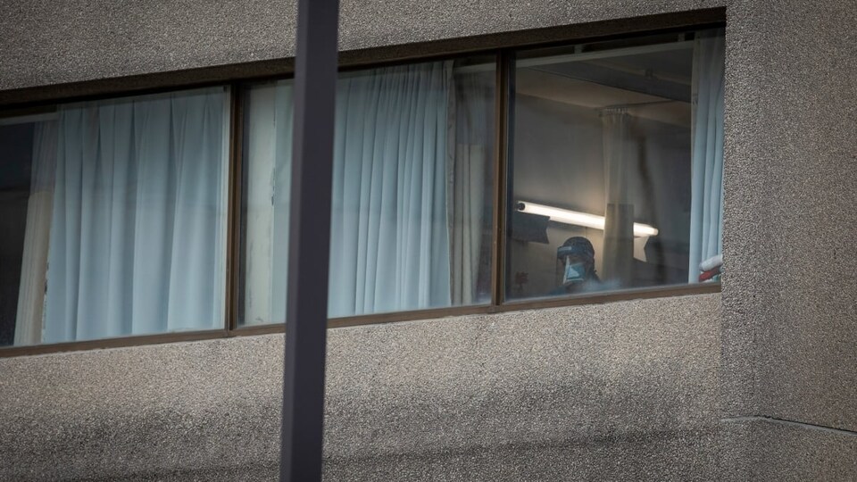 Une personne avec un couvre-visage est visible à travers une fenêtre de l'établissement.