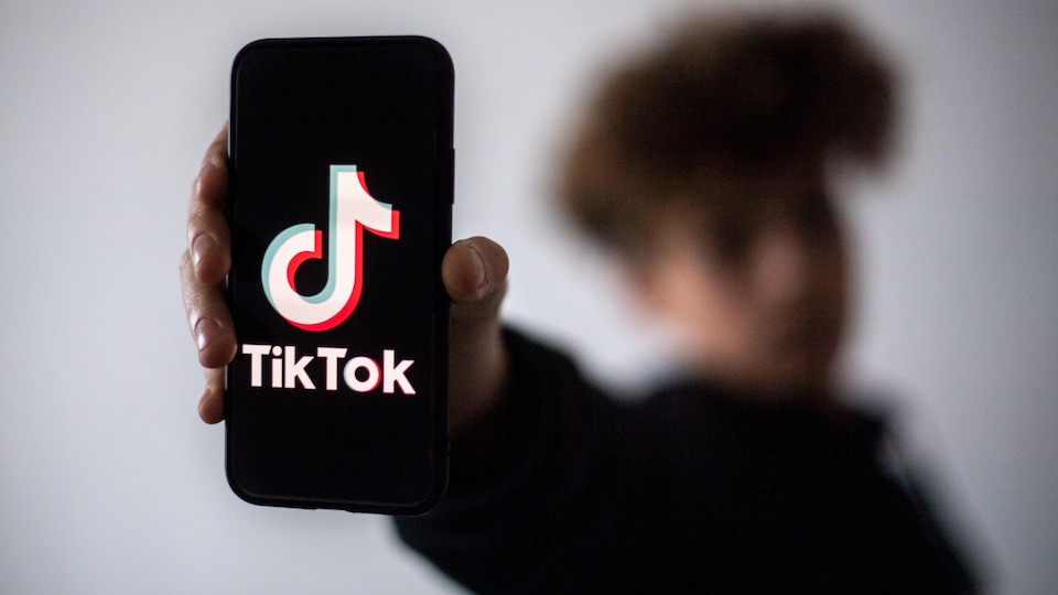 Un jeune homme flouté tient un téléphone intelligent affichant le logo de TikTok. 