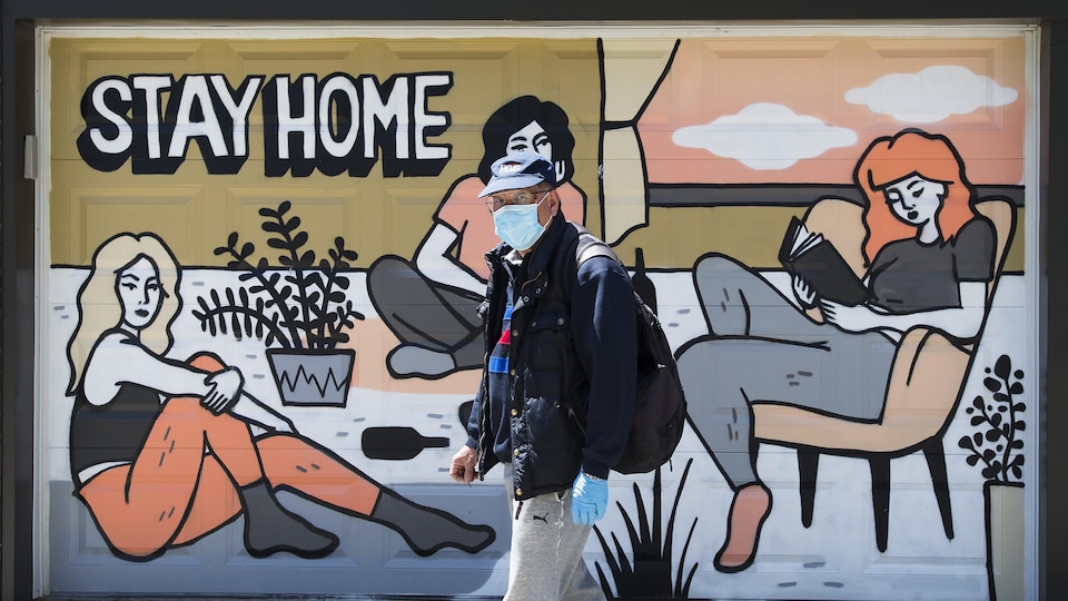 Un homme portant un masque de protection marche devant une peinture murale liée à la pandémie de COVID-19