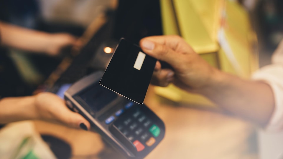 Une main tient une carte de crédit au-dessus d'un terminal de paiement.